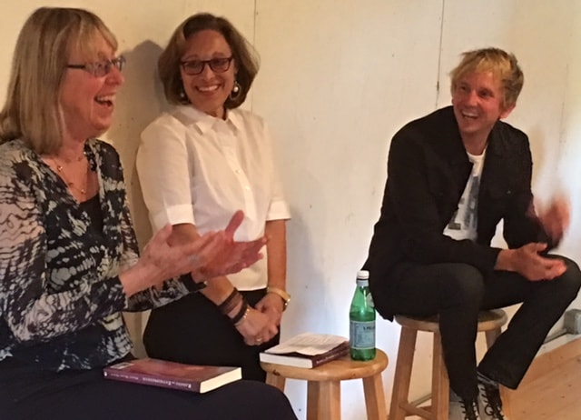 Three women sitting on stools and talking to each other.